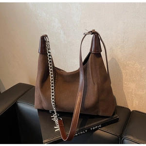 Détail du sac hobo en daim marron avec chaîne argentée et bandoulière sur canapé