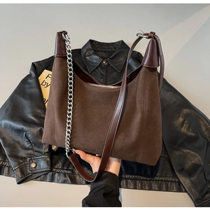 Détail d'un sac cabas en daim marron foncé avec chaîne argentée et coutures cuir