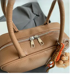 Nahaufnahme des Doppelreißverschlusses der braunen Ledertasche mit Anhänger
