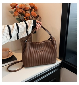 Detail view of brown pleated bucket bag with leather patch in a cozy lifestyle setting