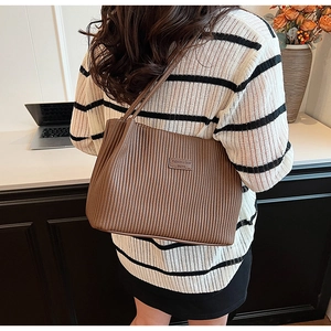 Detail of brown pleated leather tote bag with rectangular patch and slim shoulder straps