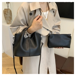 Detail view of black lychee grain leather bucket bag set on a model in beige coat