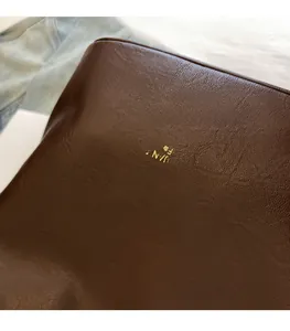 Close-up of coffee brown leather bucket bag with litchi texture and gold logo