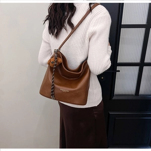 Detail of dark brown leather crescent tote bag with a cute plush bear charm on strap