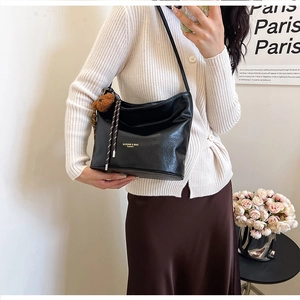 Close-up of black hobo shoulder bag with plush bear charm and woven rope detail
