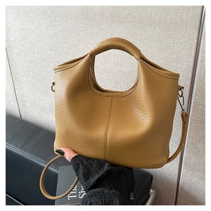 Detail of camel pebbled leather bucket bag featuring a circular cutout handle and stitching
