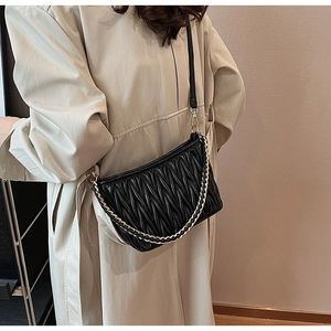 Dettaglio borsa a tracolla trapuntata nera con catena dorata su cappotto beige