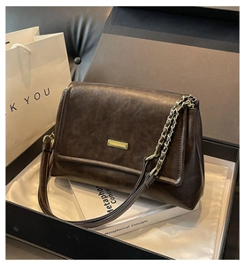 Detail view of dark brown chain strap bag with golden metal plate in a gift box setup