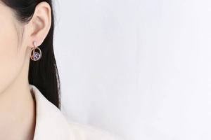 Close-up of rose gold heart-shaped purple crystal earring with diamond accents on a model