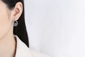 Close-up of elegant purple gemstone drop earrings worn by a model in a white suit