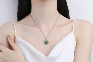 Close-up of a silver necklace with a round green gemstone pendant worn by a model