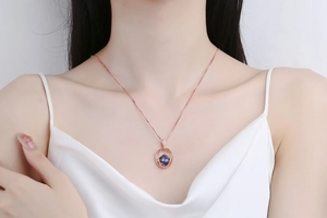 Close-up of rose gold necklace with round purple gemstone on a model wearing silk dress
