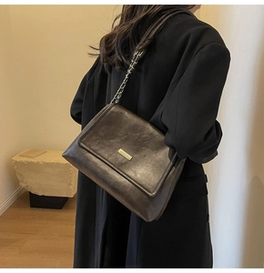 Detail of vintage brown leather crossbody bag with gold metal logo and chain strap