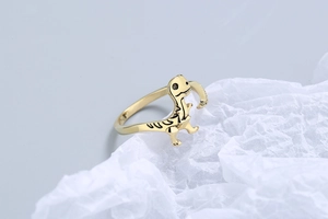 Close-up of golden adjustable dinosaur ring with black engraved details on white paper