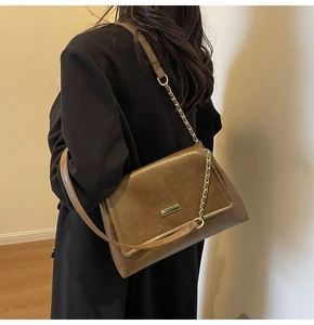 Detailed side view of a brown vintage crossbody bag with gold chain strap on a black blazer