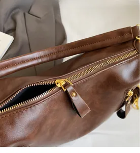 Close-up of smooth gold-tone zipper and textured brown leather on underarm tote bag