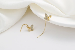Close-up of gold butterfly tassel earrings with sparkling crystals on white silk