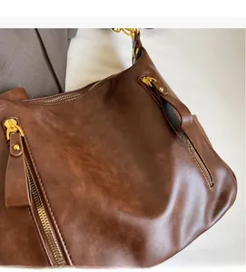 Close-up of deep brown leather shoulder bag with vintage texture and gold zippers