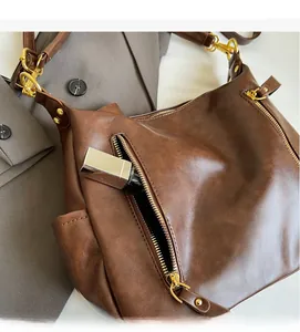 Detail of a brown leather shoulder bag featuring a functional front zipper pocket for lipstick