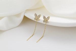 Macro shot of gold butterfly tassel earrings with sparkling cubic zirconia on white fabric
