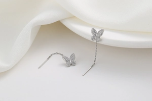 Close-up of silver butterfly tassel earrings with sparkling rhinestones on white fabric