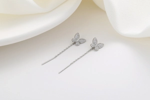 Detail of silver butterfly tassel earrings with pavé crystals on white silk background