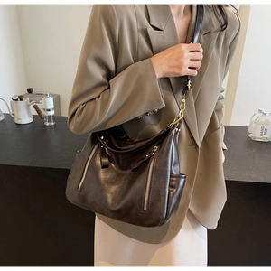Detail of dark brown leather shoulder bag featuring metallic zippers and side pocket