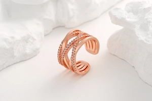 Macro shot of rose gold criss-cross ring with pavé zircons on white rock texture