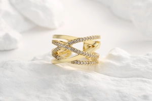 Macro shot of gold-plated criss-cross ring with pavé diamonds on a white stone base