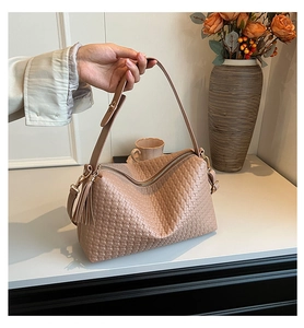 Détail du sac Boston tissé beige avec pompon élégant et finitions métalliques dorées