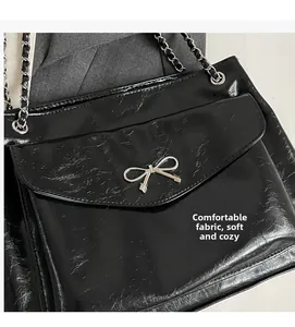 Close-up of black glossy pleated tote with silver bow and woven chain strap details