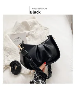Détail du sac plissé noir avec poignée tressée et bandoulière réglable sur tissu blanc