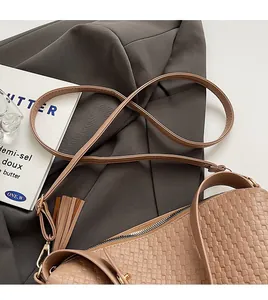 Gros plan d'un sac tressé marron clair avec fine bandoulière et détail de pompon