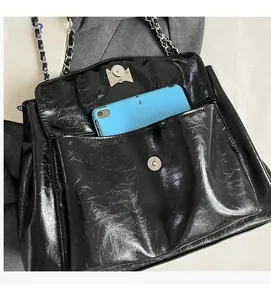 Detail of black crinkle patent leather tote bag with silver chain strap and front pocket
