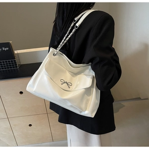 Detail of white tote bag featuring a metallic silver bow and chain shoulder strap