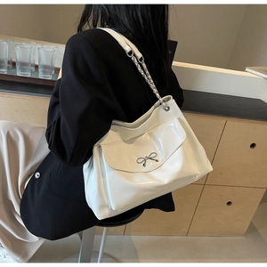 Close-up of white glossy leather tote bag with silver metal bow and chain strap