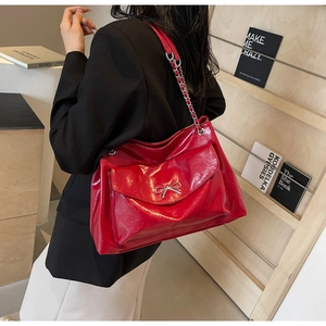 Detail of red patent leather shoulder bag with silver bow buckle and chain strap