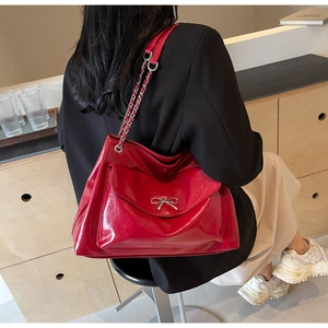 Detail of red patent leather tote bag with silver metal bow and chain strap on model