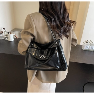Detail of glossy black tote bag featuring a silver metal bow and chain shoulder strap