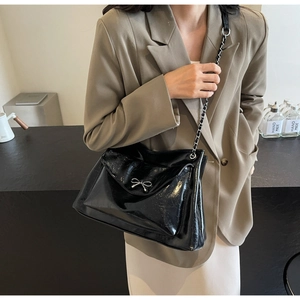 Detail of glossy black leather tote bag featuring silver bow accent and chain strap