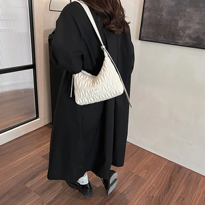 Close-up detail of white pleated crescent bag texture on model wearing black coat
