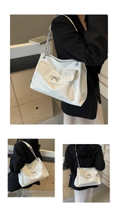 Detail of white glossy tote bag with metal bow accent and chain shoulder strap design