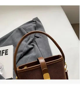 Detail of a brown suede bucket bag featuring a vertical golden metal lock and round handle