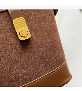 Macro detail of brown suede texture, leather stitching and golden metal lock on the bucket bag