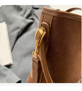 Detail of brown bucket bag showing suede stitching and glossy gold hardware hooks