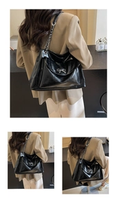 Detail of glossy black tote bag featuring a silver metal bow and chain leather strap