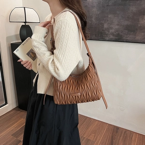 Detailed side view of caramel pleated leather underarm bag with Matelasse style texture