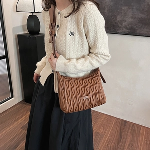 Close-up of brown pleated leather shoulder bag featuring a decorative bow on the strap