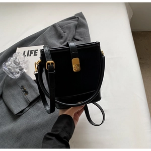 Detail of a black bucket bag with gold hardware and fine shoulder strap on a modern background