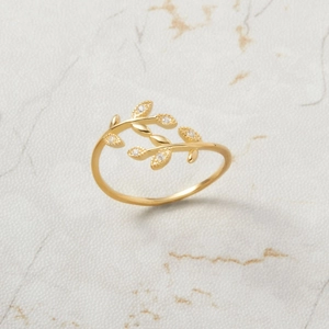 Macro detail of gold olive leaf ring featuring sparkling zircon crystals on marble